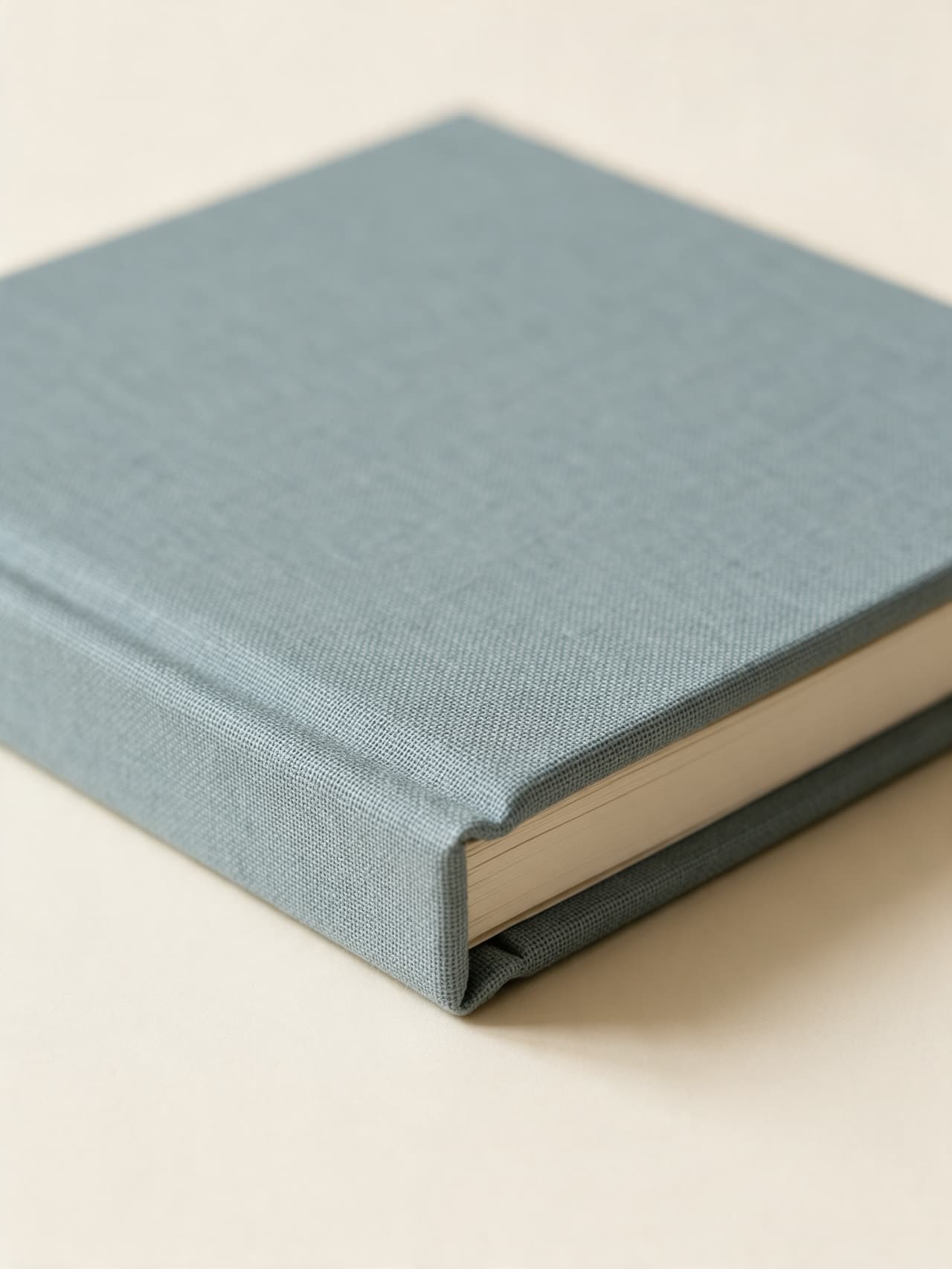 Close up of the corner of a dusty blue linen album: the weave of the cloth folded over the board and the thick cream page block below