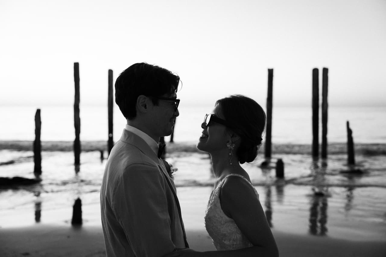 Black and white silhouettes of a couple facing each other among old jetty posts