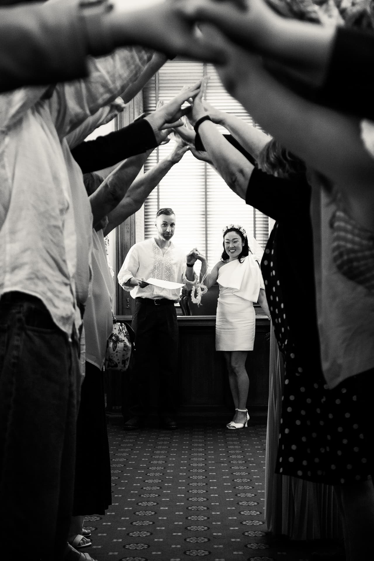 Black and white photo of guests forming a tunnel of raised hands for the couple