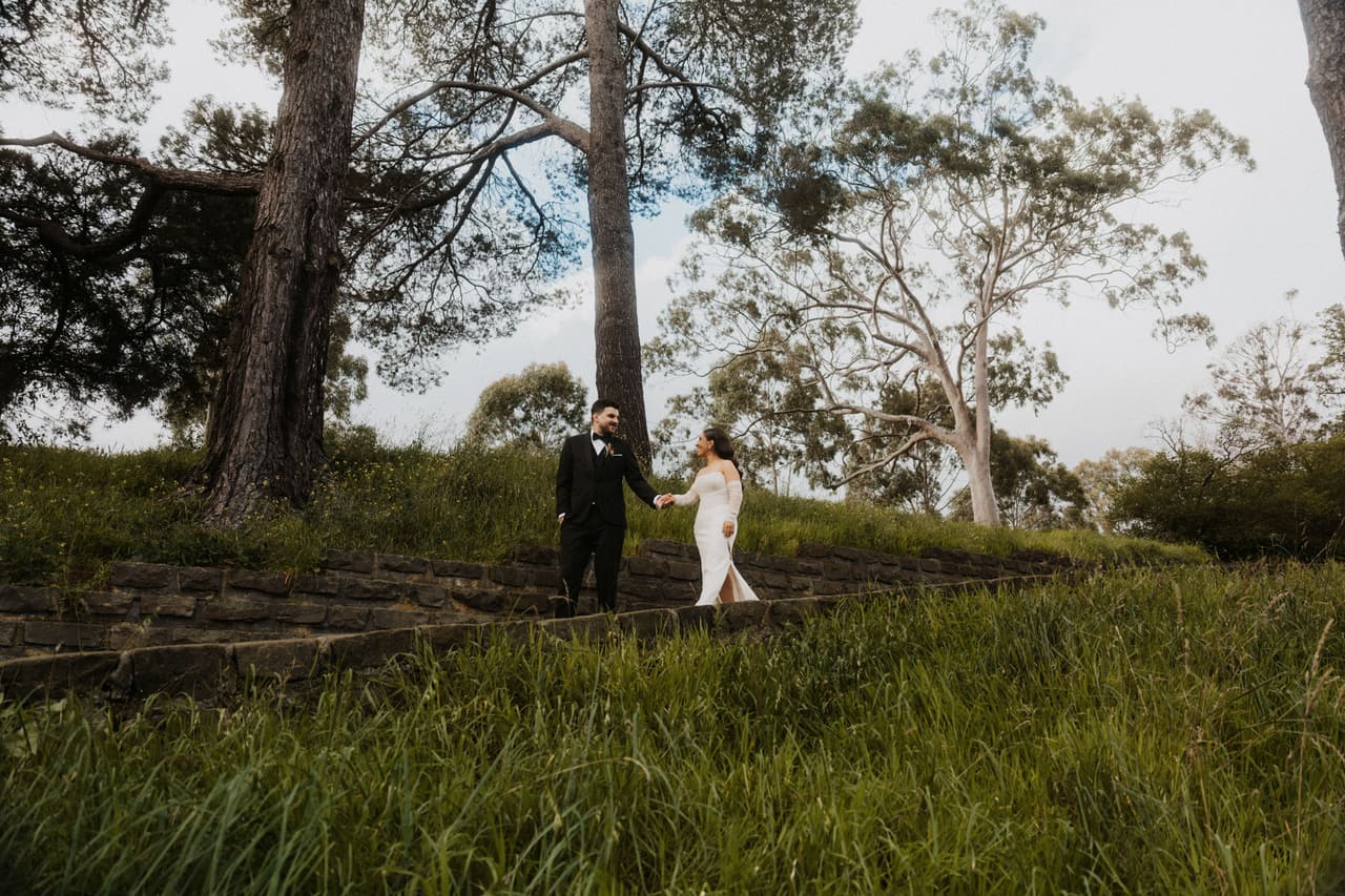 A couple walking towards each other through long grass beneath tall gum trees