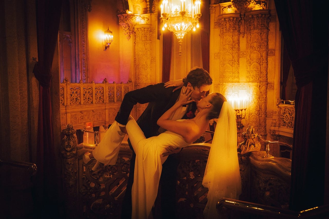 A groom kissing the bride in a candlelit, wood-panelled room