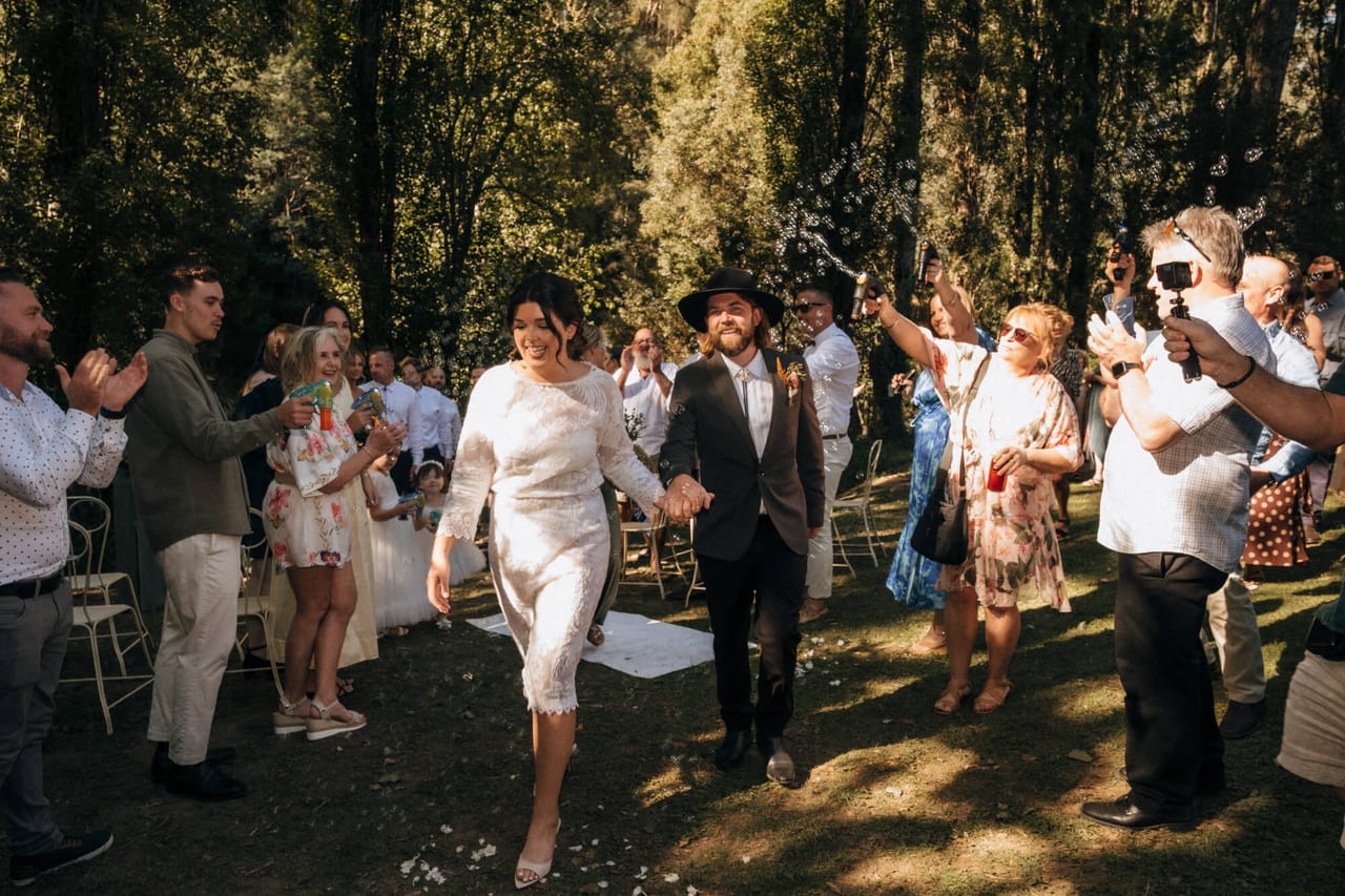 A couple walking out through confetti and cheering guests in a sunlit garden