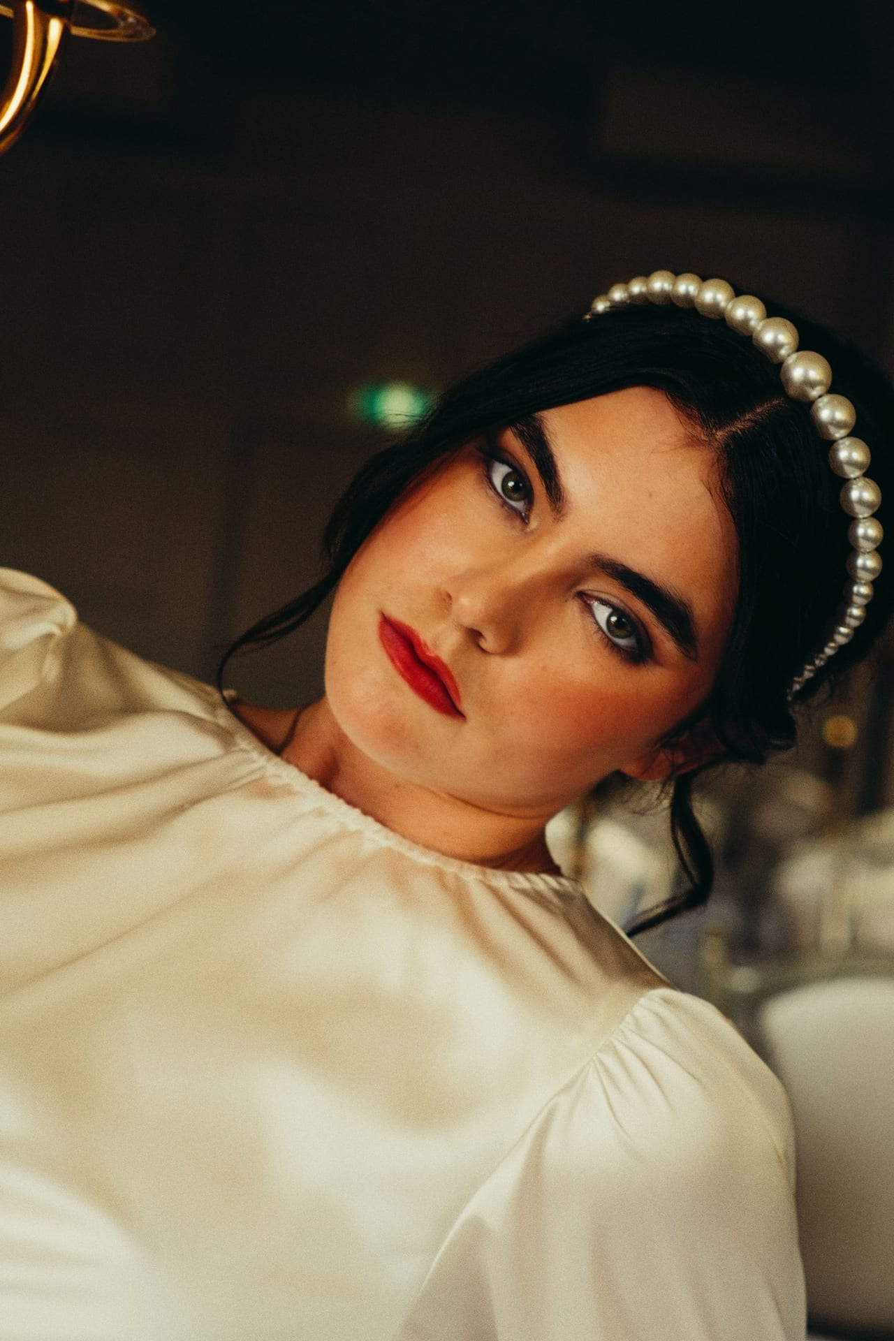 A bride in a pearl headband and red lipstick looking up at the camera