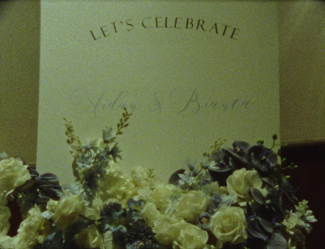 The Let's Celebrate sign at The Imperial Hotel behind white roses and blue flowers