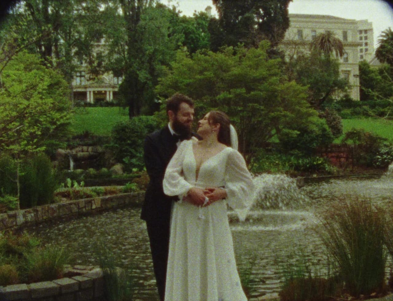 A kiss beside the fountain in the gardens, the city behind the trees