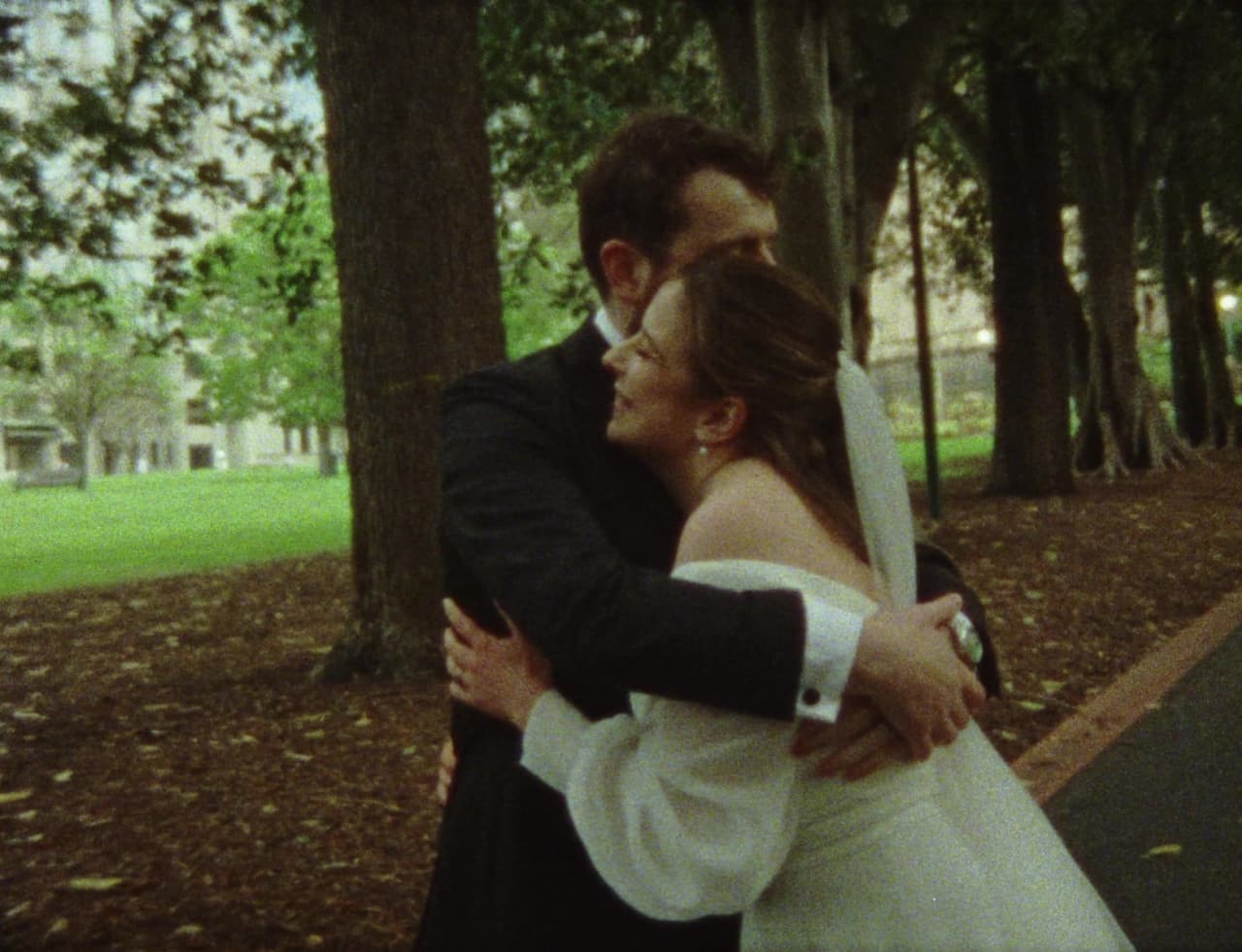 Aidan holding Bianca close under the elms, both of them laughing