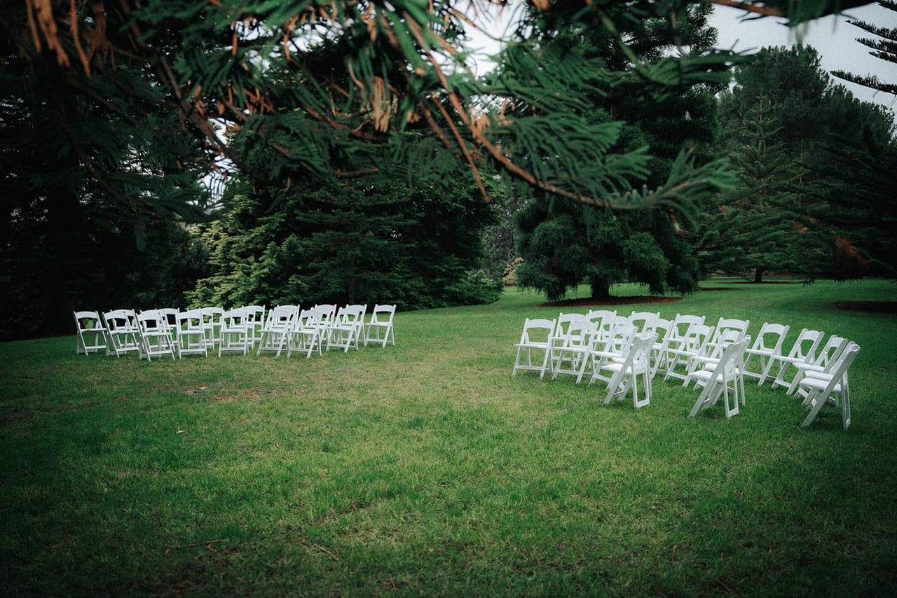 White folding chairs set out in a curve on the lawn under the pines before the guests arrive