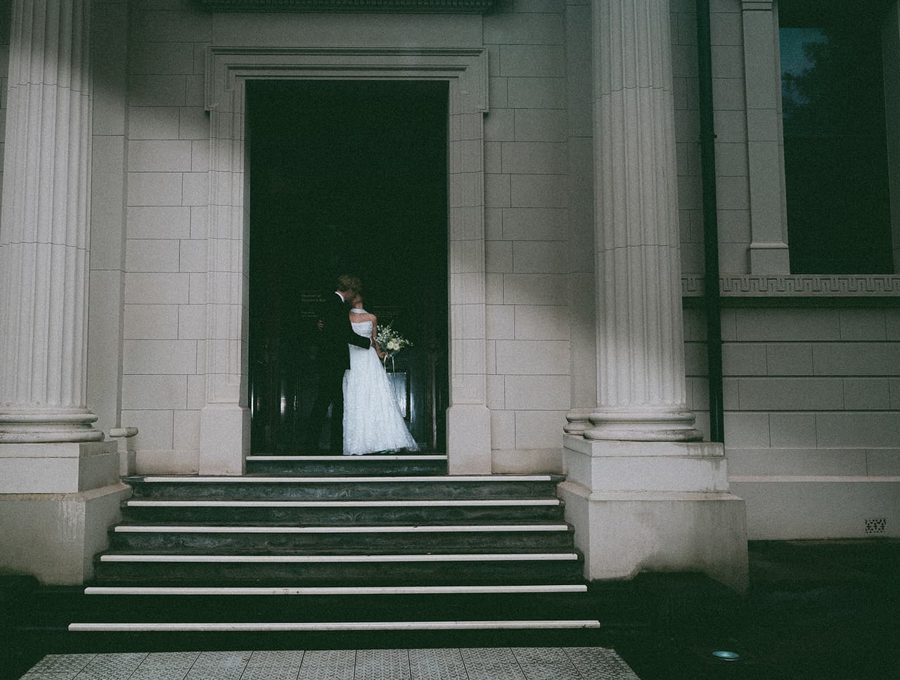 Eli and Charlotte embracing in the doorway of the Museum of Economic Botany, its columns and stone steps in front