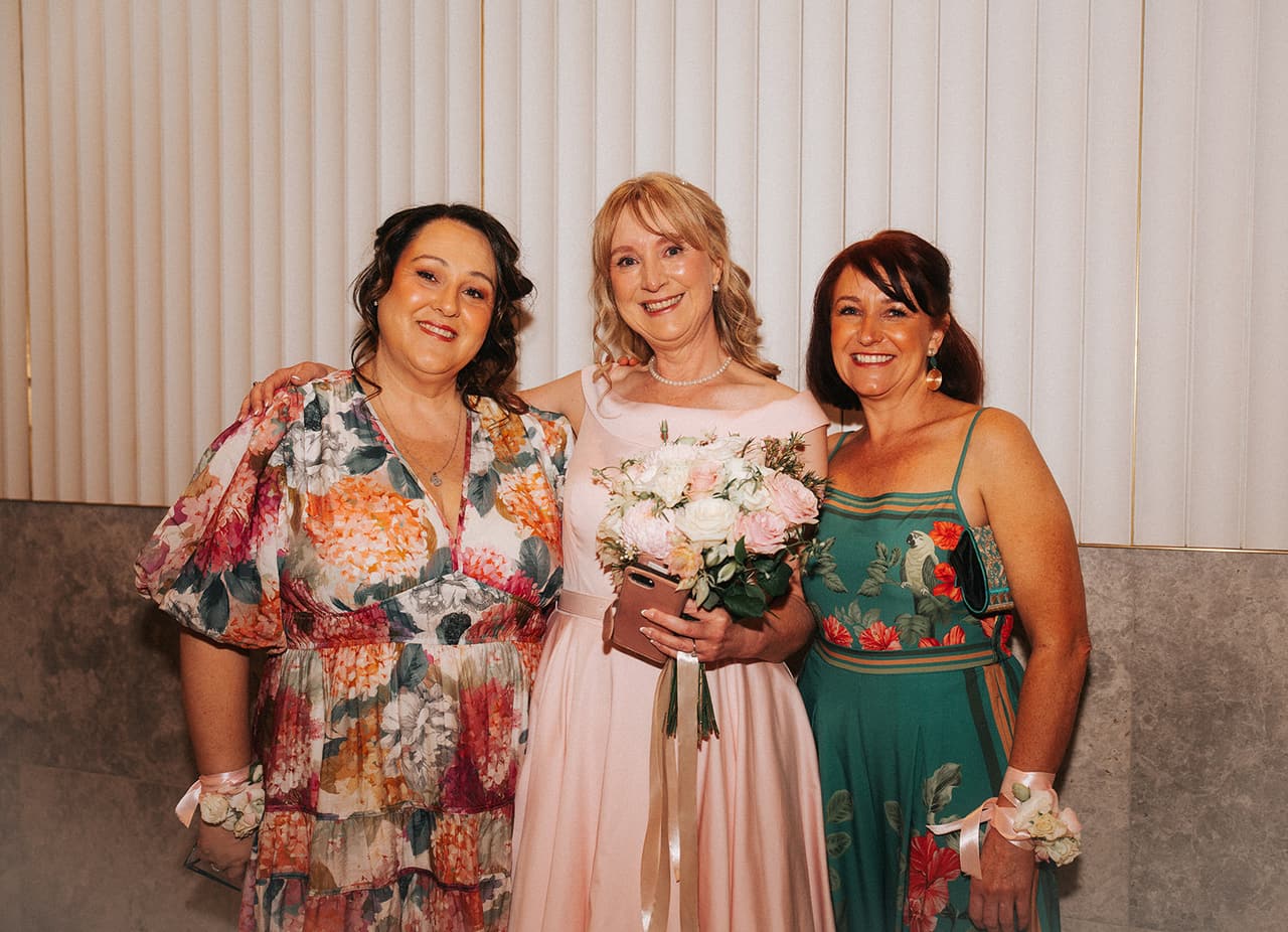 Terrie with two friends in bright dresses against the fluted white wall and stone panels of the registry foyer