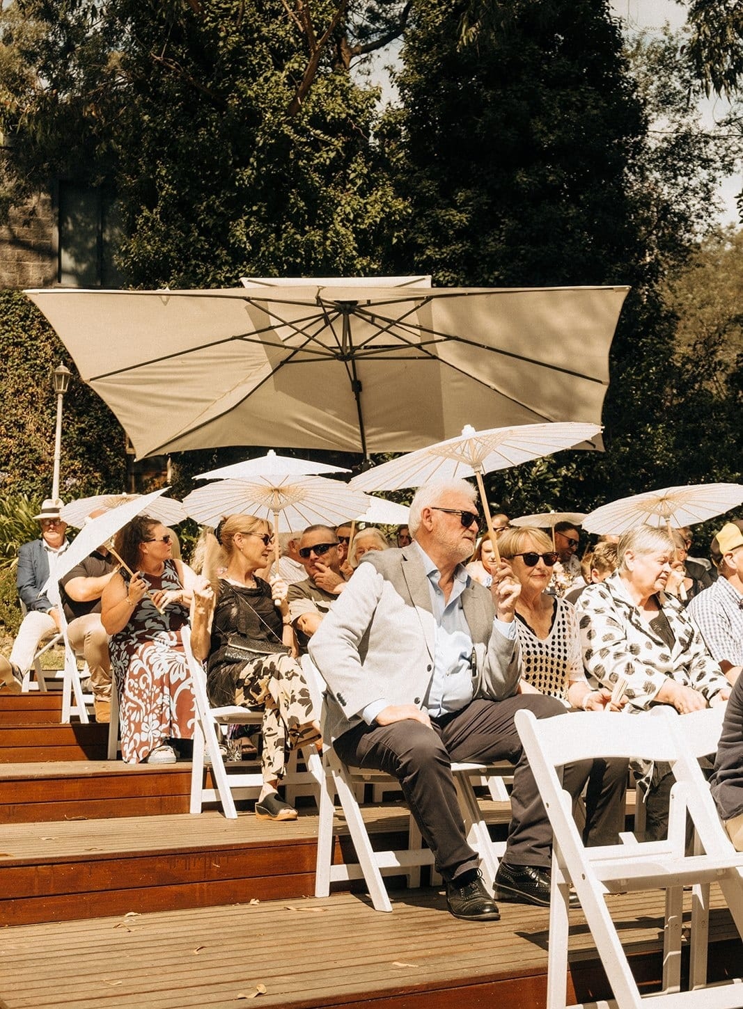 Guests seated on the tiered ceremony deck under white parasols and market umbrellas