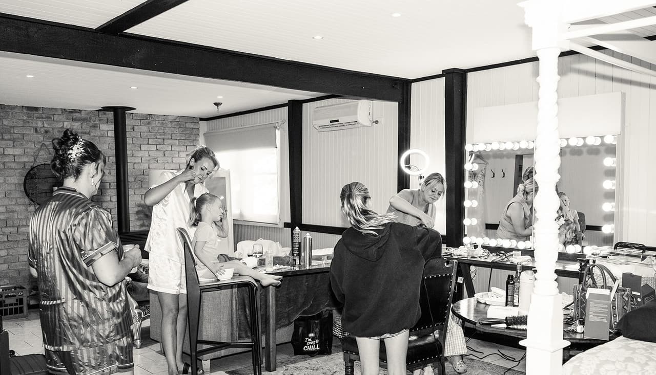 Black and white photo of the getting ready room, with its lit mirrors, timber beams and a door to the garden