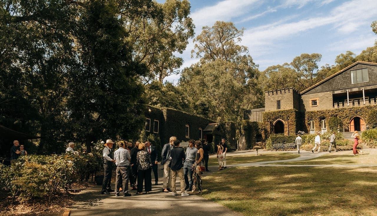 Guests gathering on the lawn and driveway before the ceremony, the castle among the gums behind them