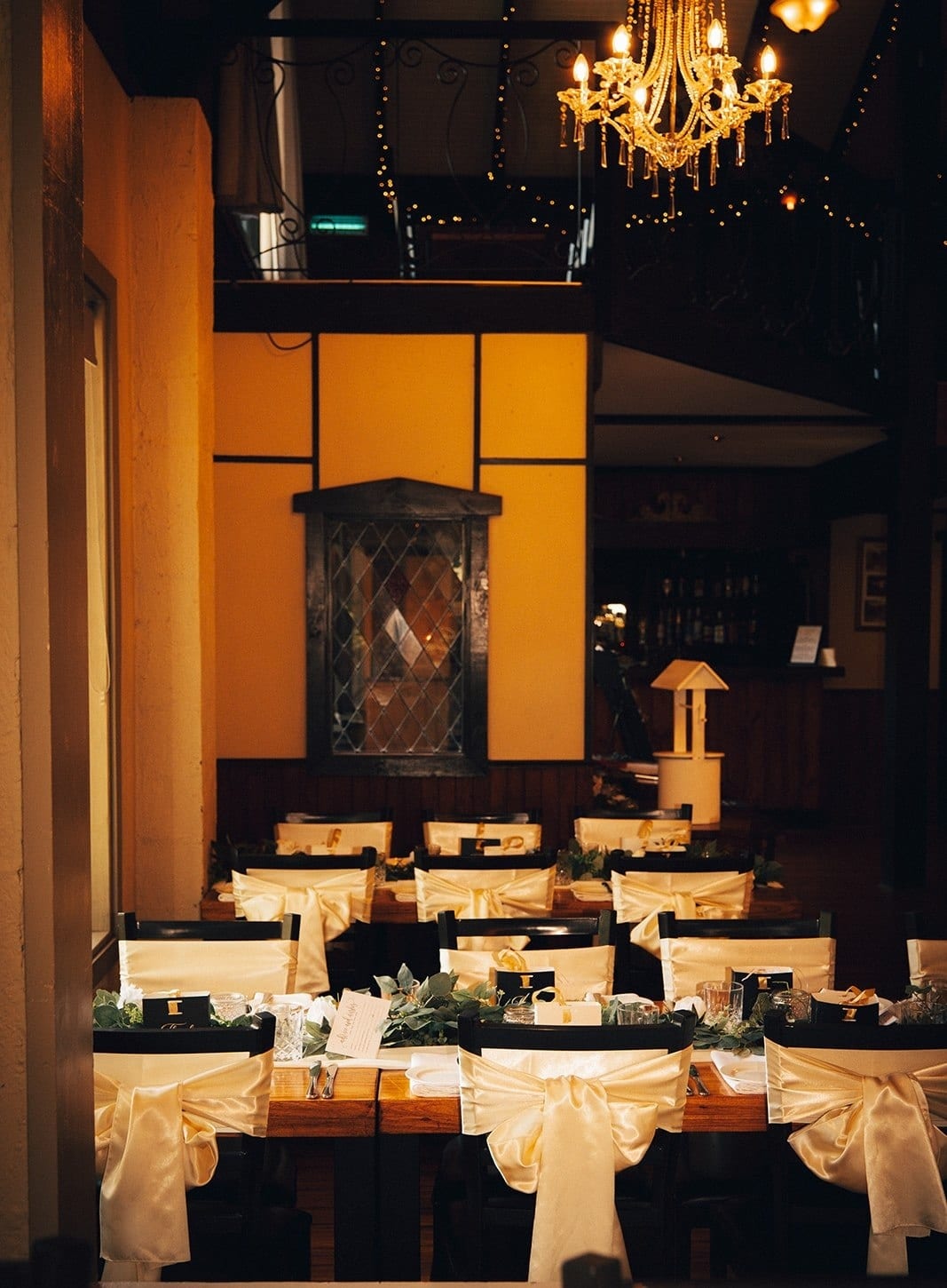 The reception hall under a chandelier, long tables set and the bar at the back