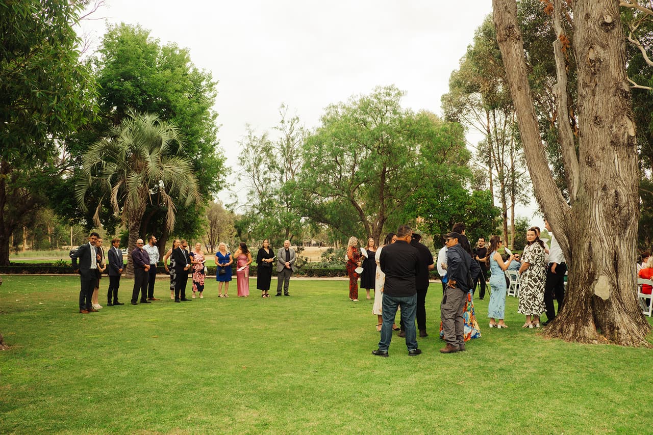 Guests gathering on the lawn under the old gums and palms before the ceremony