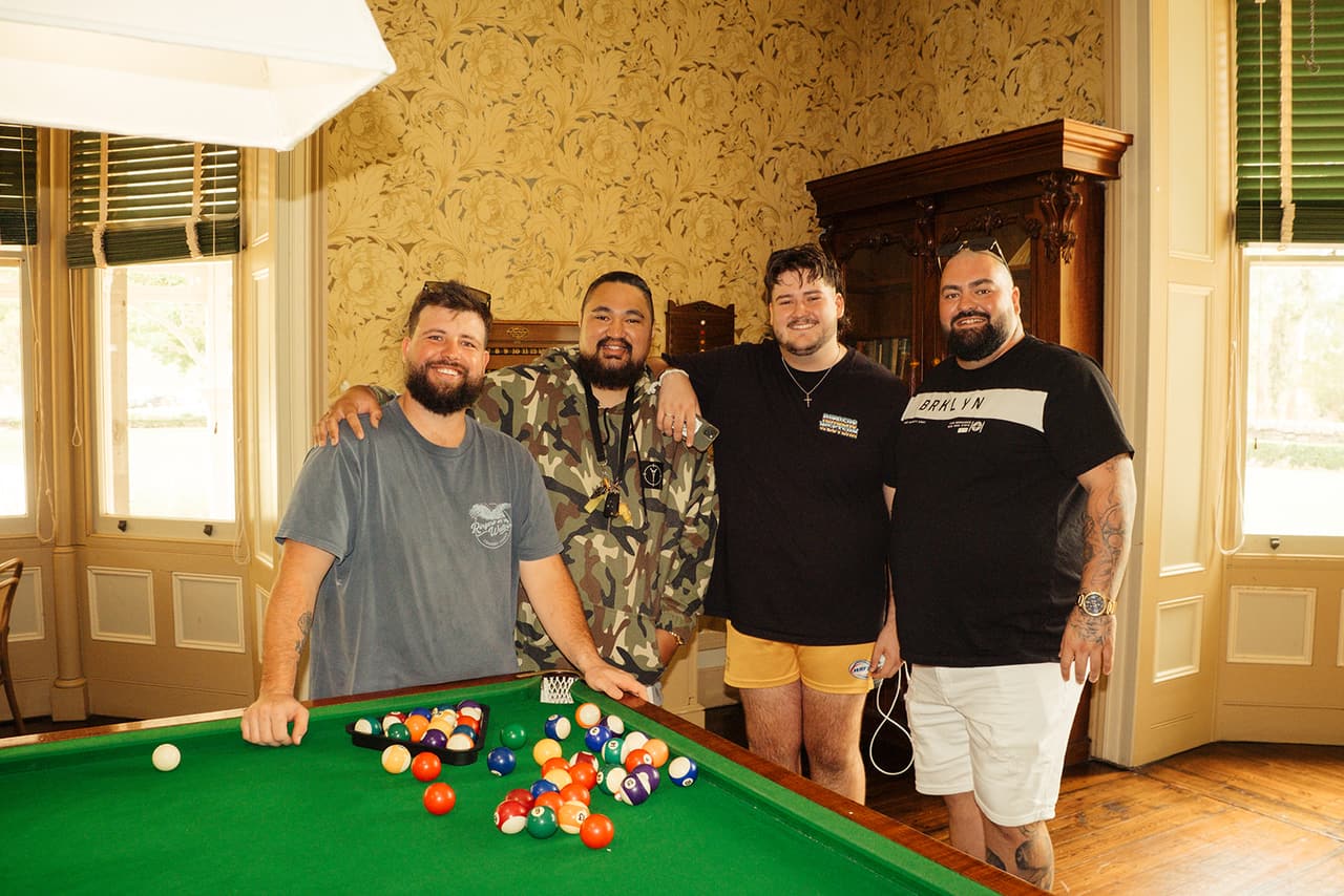 Four of the men around the pool table in the billiard room, gold patterned wallpaper and green blinds behind them