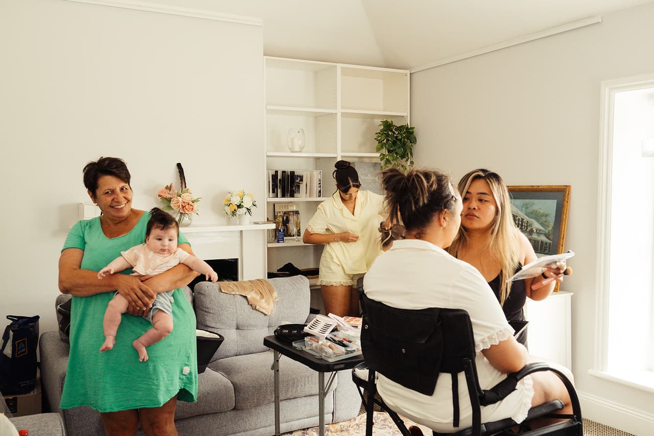 The white bridal room with built-in bookshelves, a grey sofa and a tall window, busy with hair and makeup