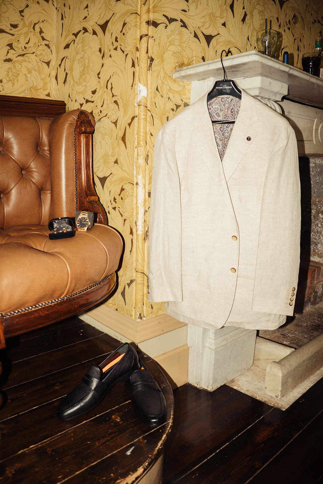Bronson’s cream jacket hanging beside a leather chesterfield chair against gold patterned wallpaper