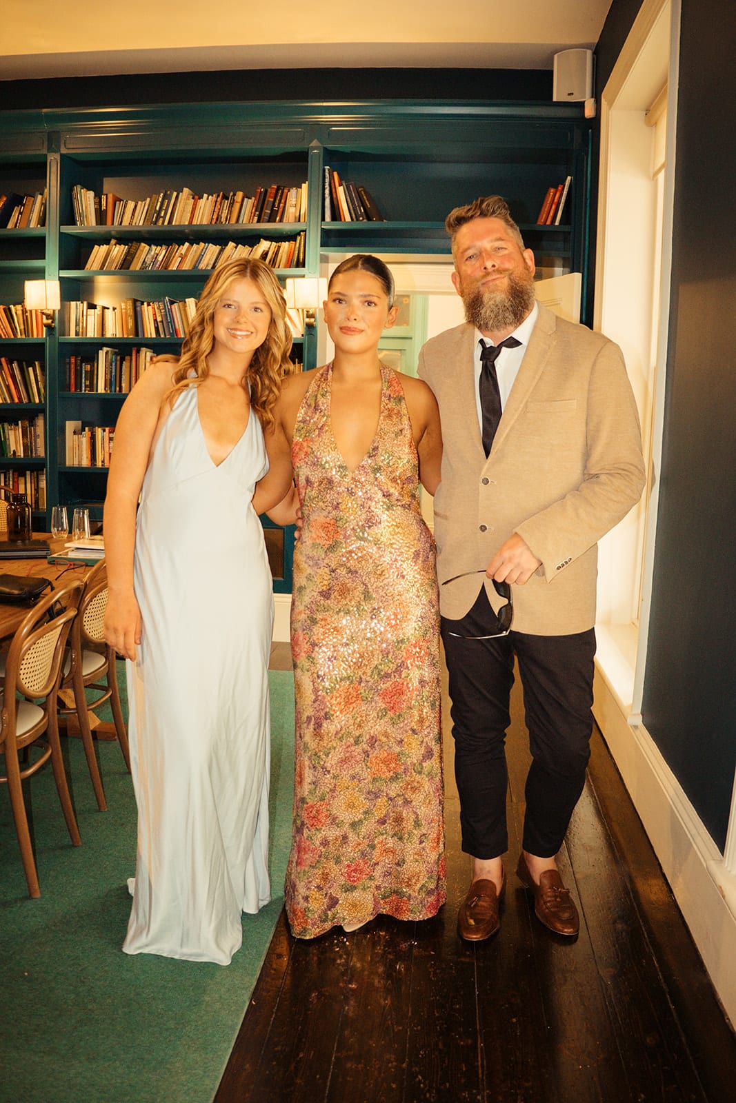 Three guests dressed for the day in the library, its walls lined with dark green bookshelves