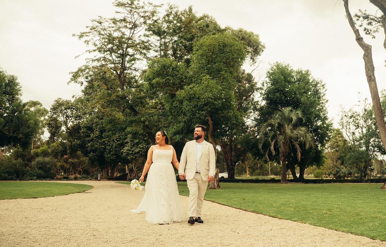 Karina and Bronson walking hand in hand along the curved gravel drive between the lawns
