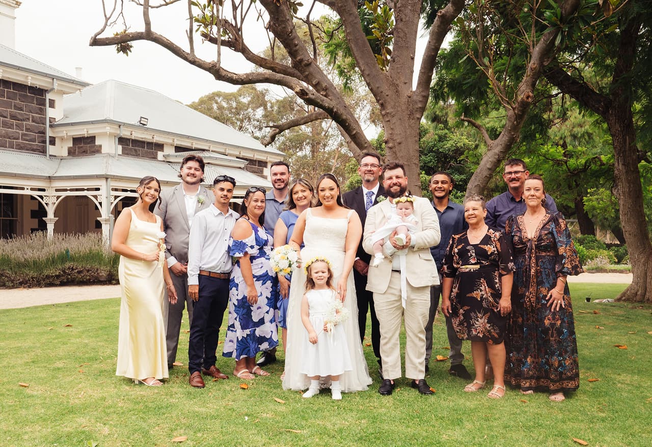 A family group on the front lawn under a spreading old tree, the homestead’s veranda behind them