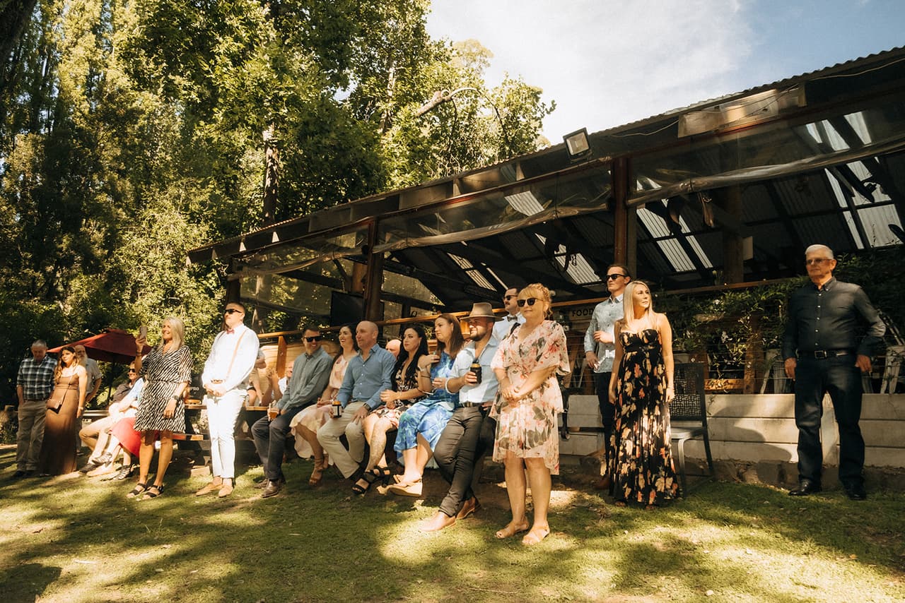 Guests waiting on benches in the dappled shade, the timber reception pavilion behind them