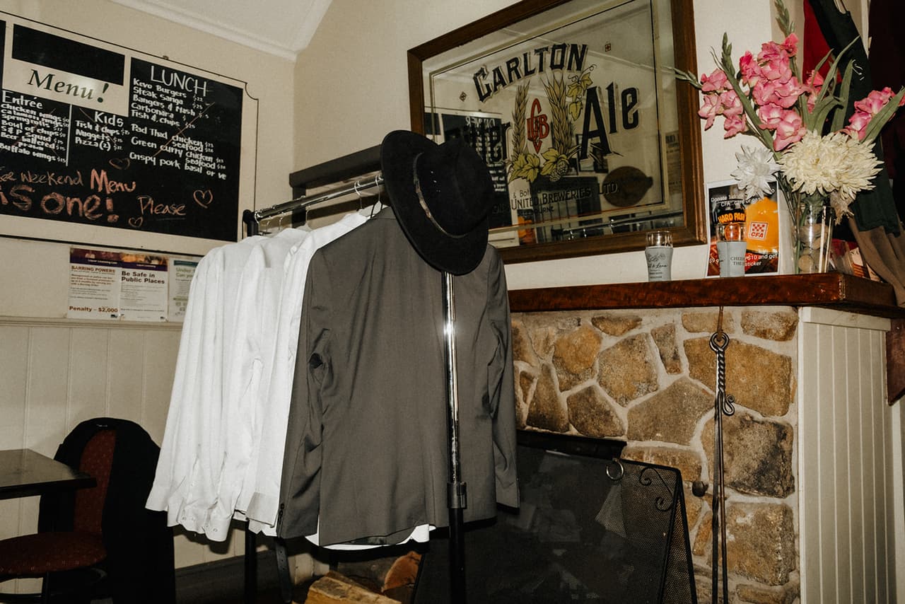 White shirts, a grey jacket and a black wide-brimmed hat hanging by the stone fireplace in the pub, a Carlton Ale mirror above