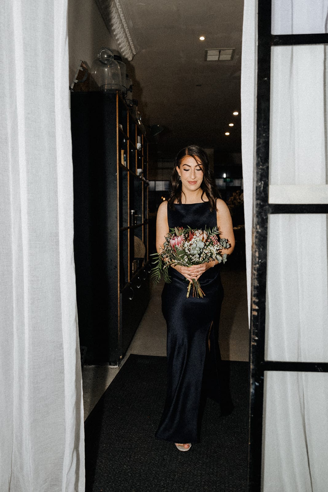 A bridesmaid walking into the ceremony through black steel doors hung with white curtains