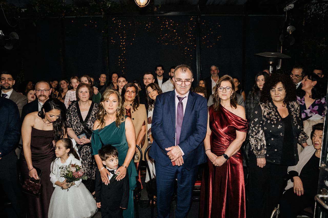 Guests standing in the covered courtyard under fairy lights as the flower girl and page boy reach the front