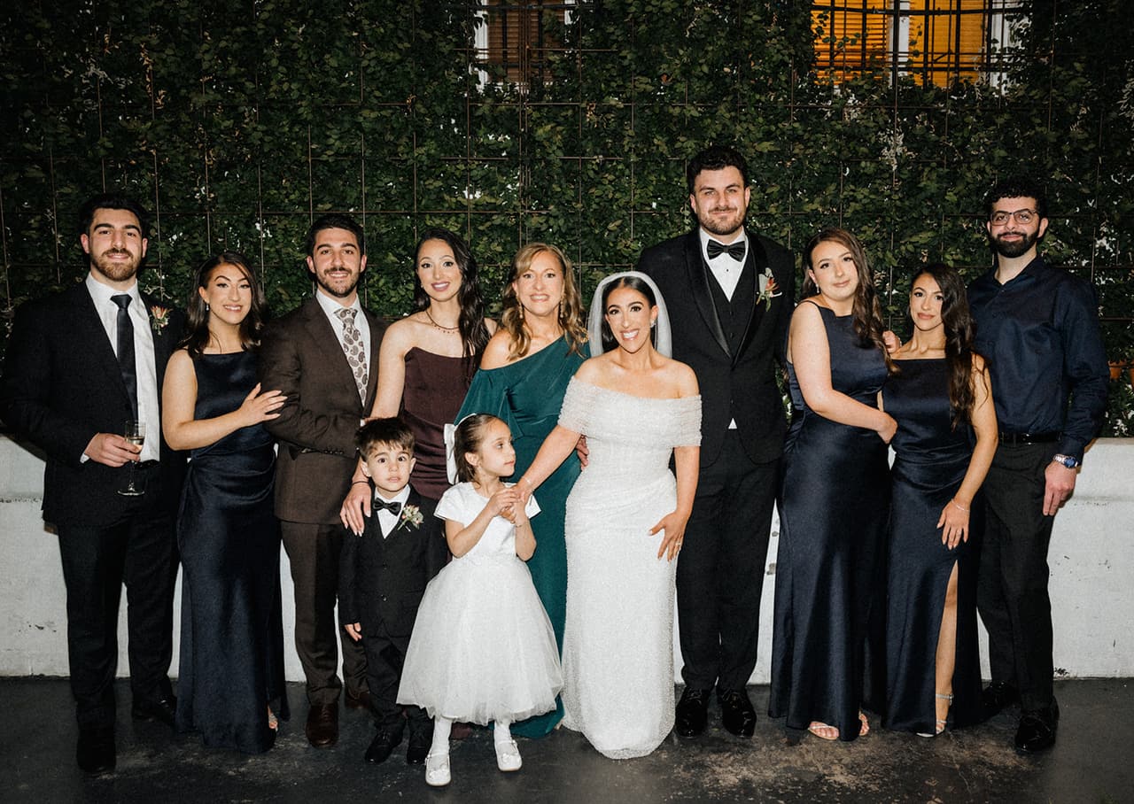 George and Tia with family and the bridal party in front of the green garden wall of the courtyard
