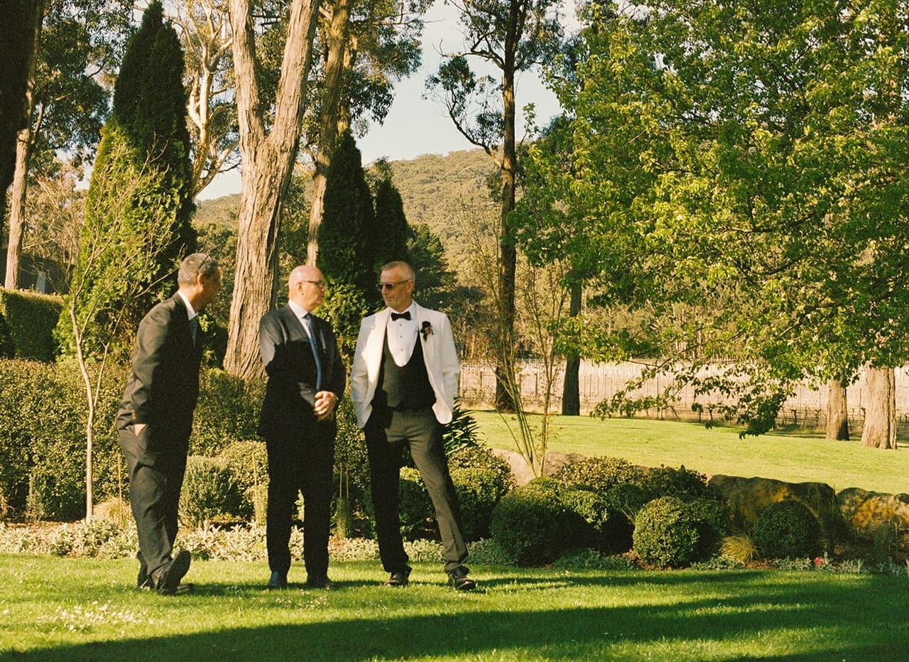 Gareth and two men waiting on the lawn by clipped hedges and tall cypresses, on 35mm film