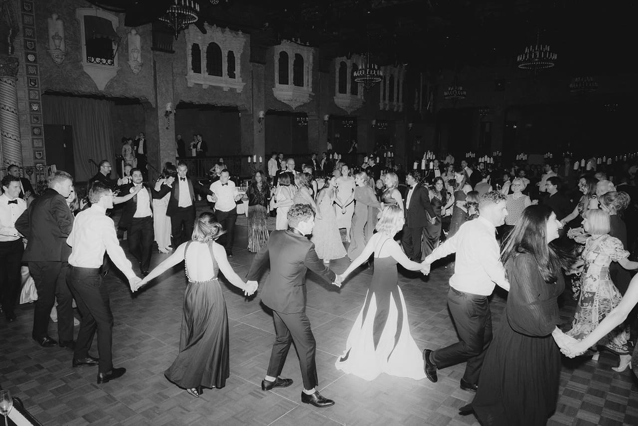 Black and white photo of guests dancing in a circle around the couple