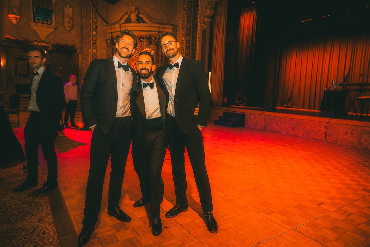Nick with two friends in dinner suits on the dance floor under red light