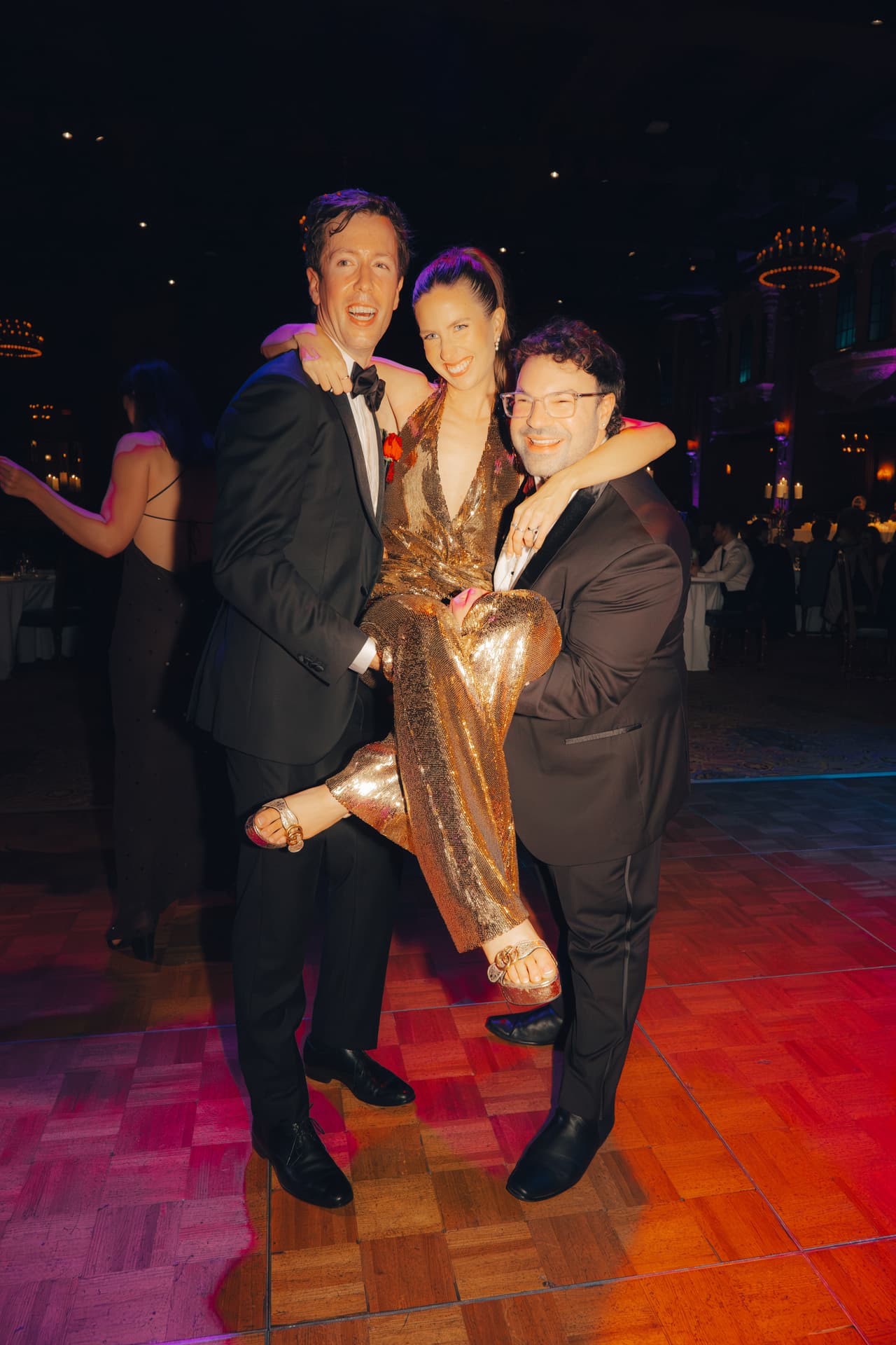 Nick and a friend holding Kira up between them on the dance floor