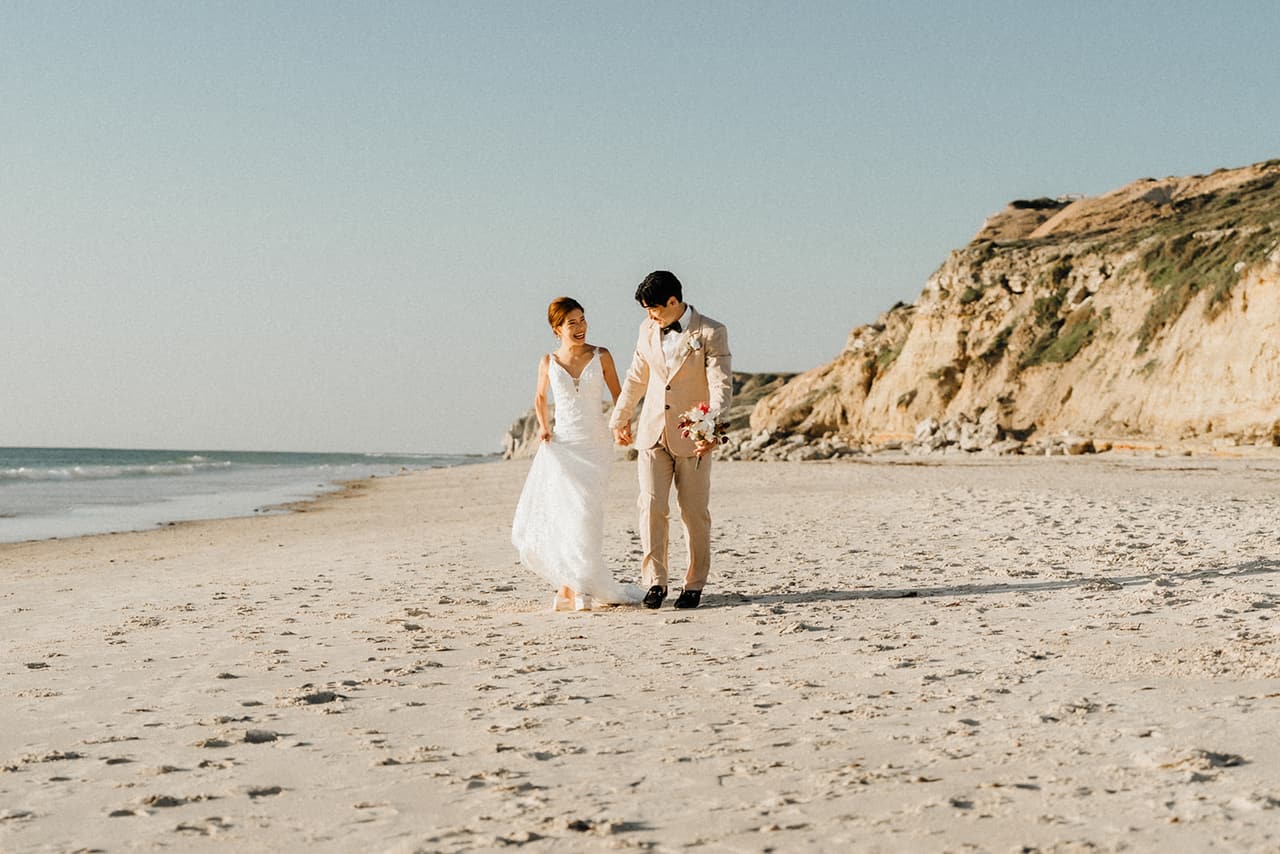 Sayuri and Shuto walking along the wide beach, the golden sandstone cliffs behind them