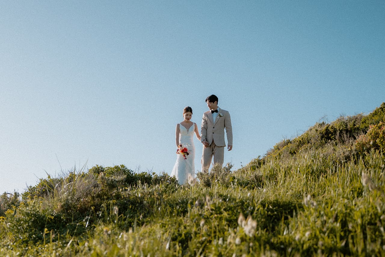 Sayuri and Shuto standing on top of the grassy clifftop under a clear blue sky