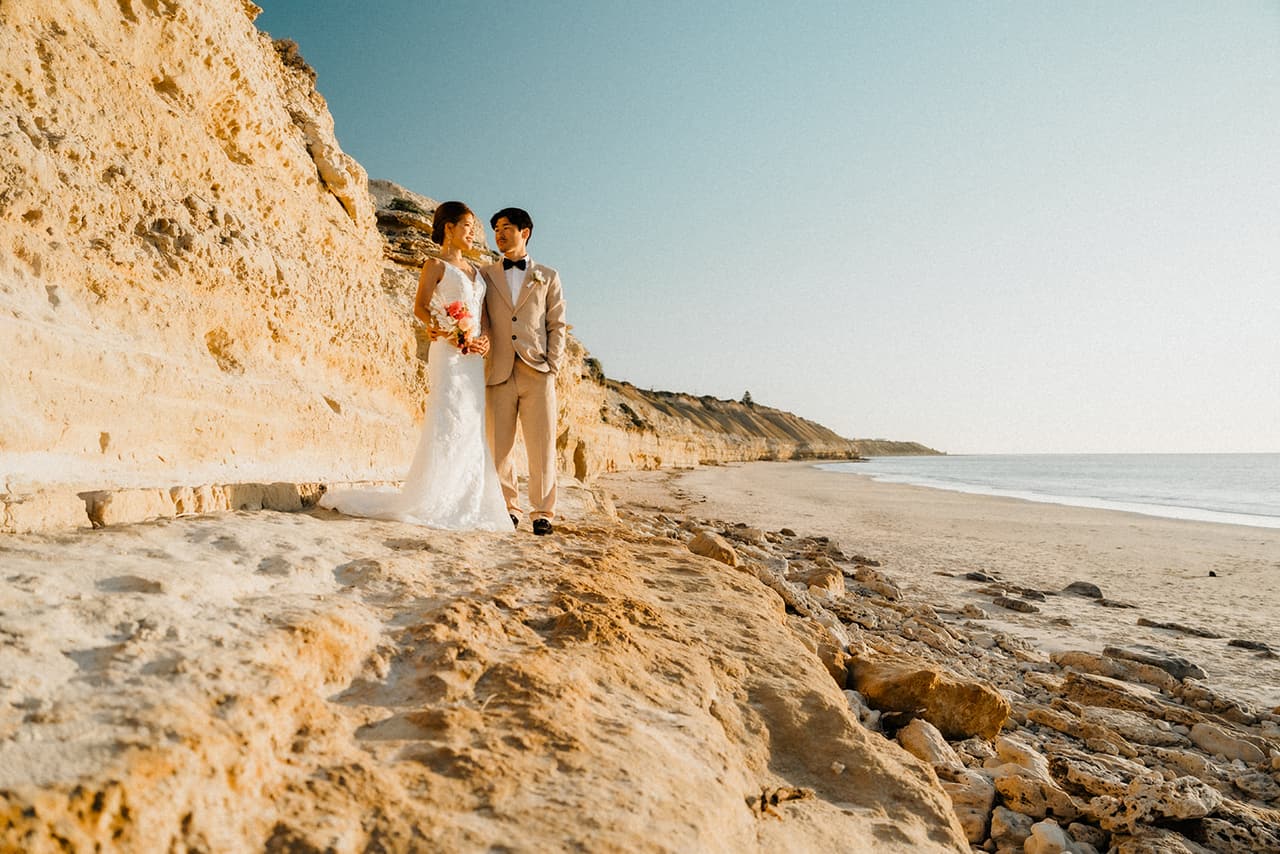 Sayuri and Shuto on the rock shelf at the foot of the golden cliffs, the beach and the sea beside them