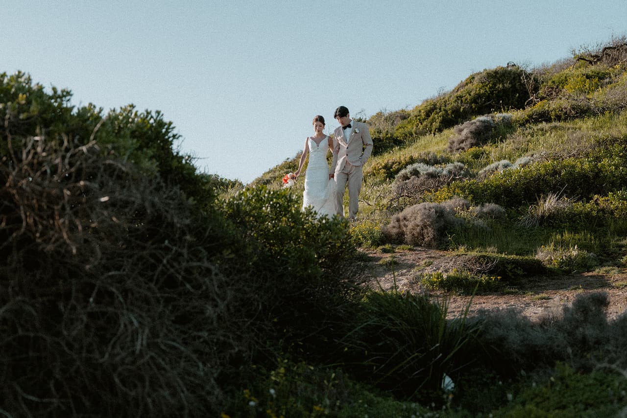 Sayuri and Shuto walking down the clifftop slope between low coastal bushes