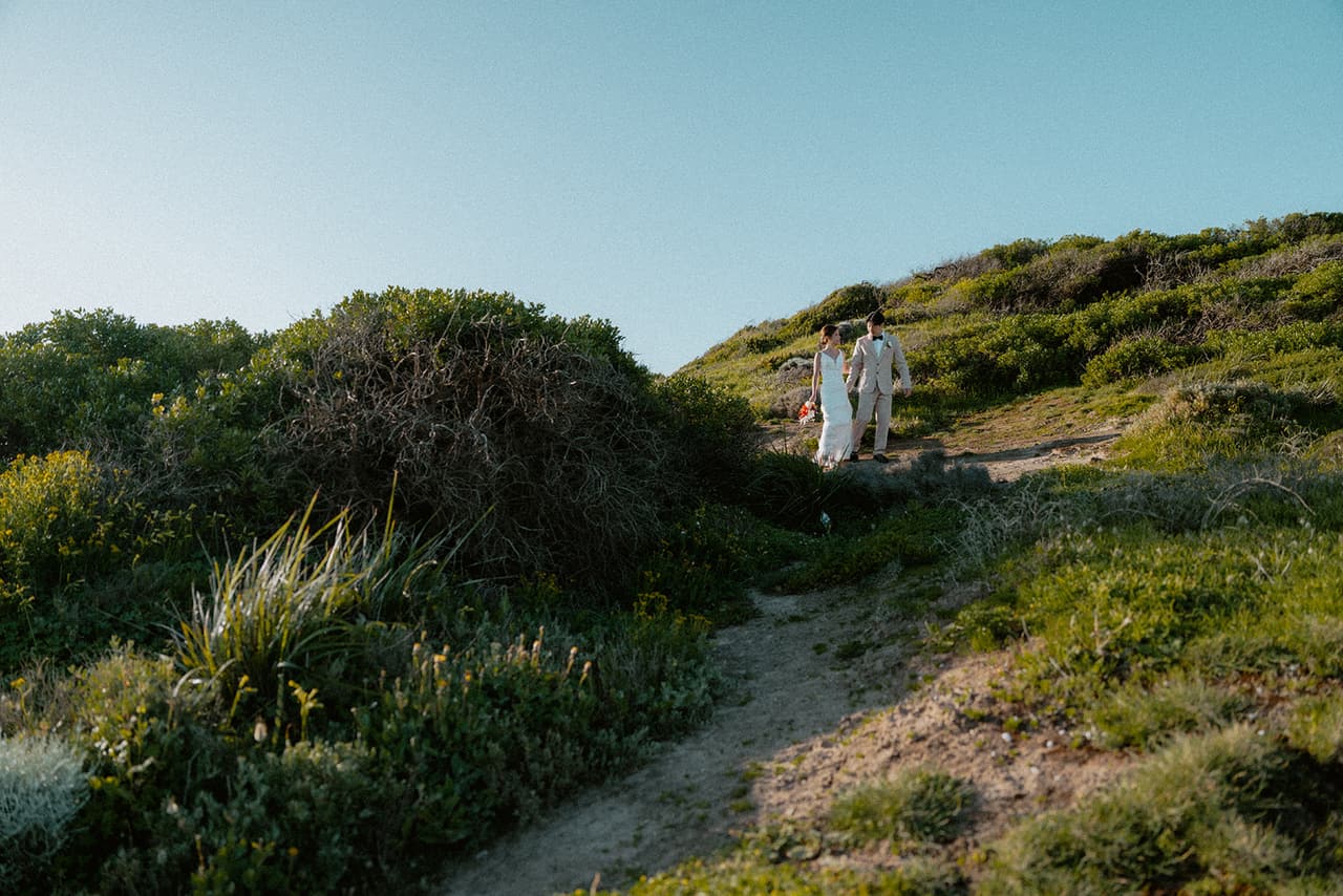 A sandy track winding up through the coastal scrub on the clifftop, Sayuri and Shuto at the top