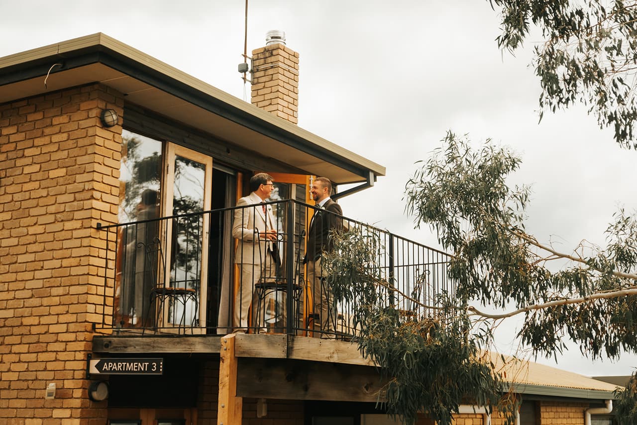 The groom’s party on the balcony of a brick apartment building among the gum trees
