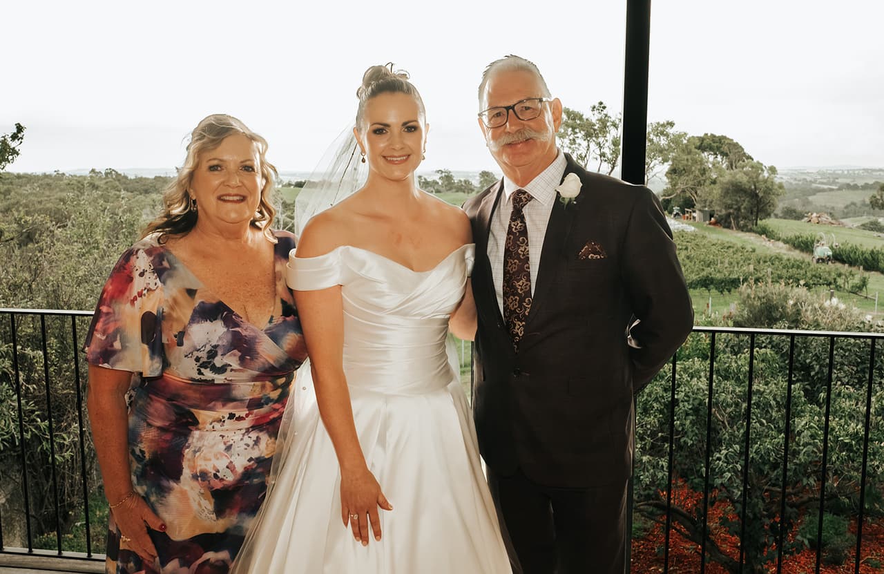 Jessica with her mum and dad on the balcony outside the bridal room, the vines and green hills behind them