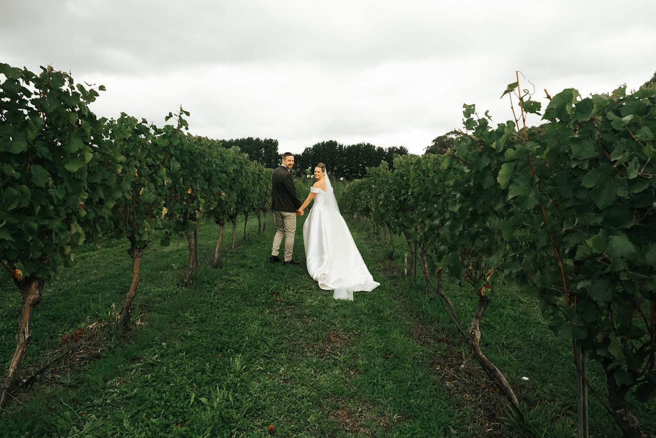 Jessica and Max standing far down a grassy row between the vines under a grey sky