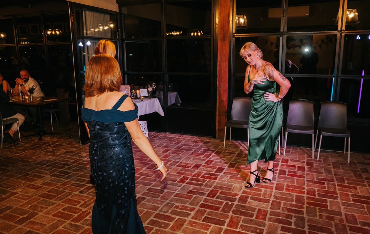Two guests dancing on the empty brick dance floor at night, chairs pushed back against the windows