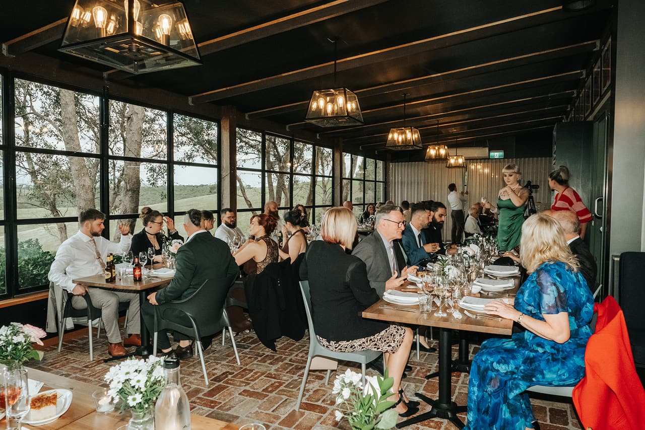 Guests at dinner along the windows of the reception room, lantern pendant lights overhead