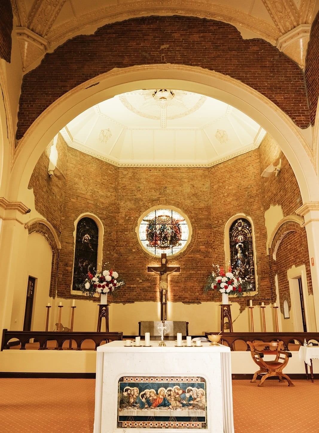 The marble altar with its Last Supper panel, the round stained glass window and the brick apse behind it