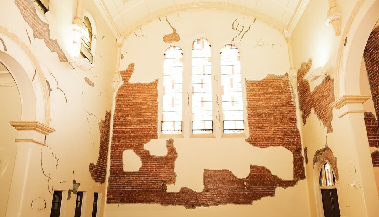 Cream plaster opened up in patches to the red brick beneath, under three tall windows