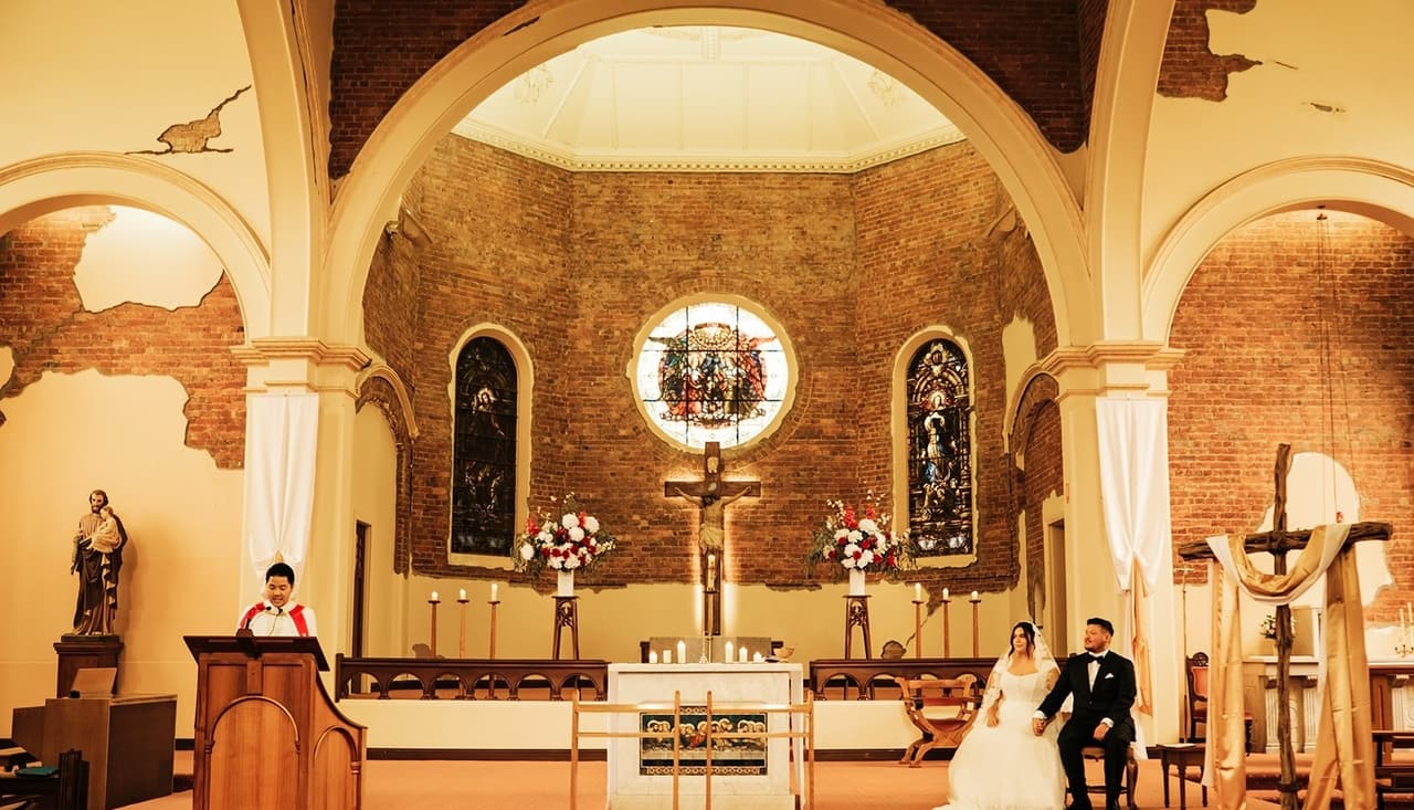 The couple seated in the sanctuary during a reading, seen across the width of the church