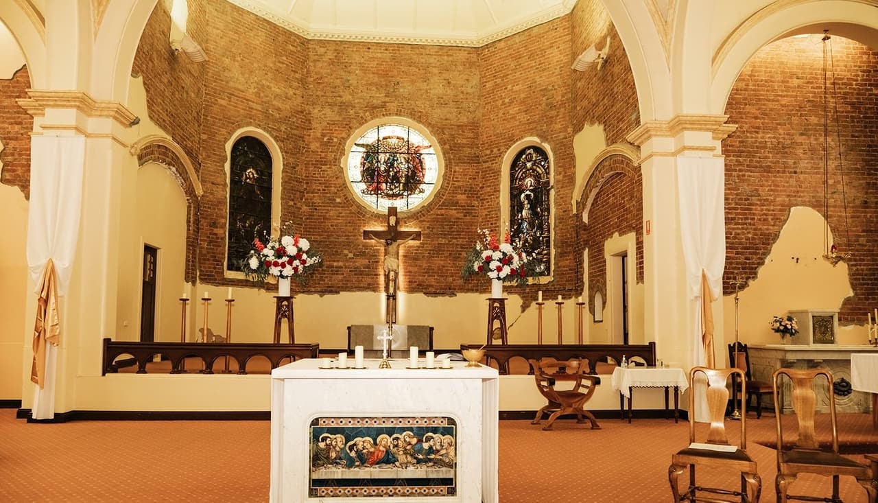 The empty sanctuary before the ceremony, with red and white flowers either side of the crucifix