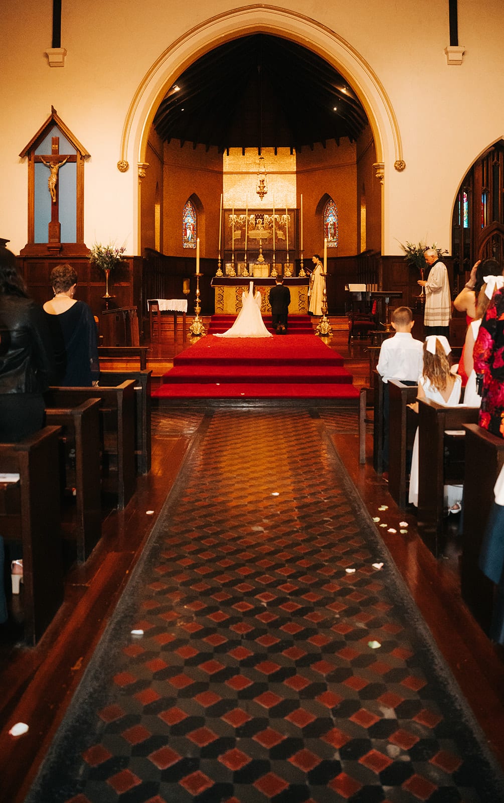 The tiled aisle running between the pews to the red carpeted sanctuary, Bianca and Aidan kneeling at the altar far ahead