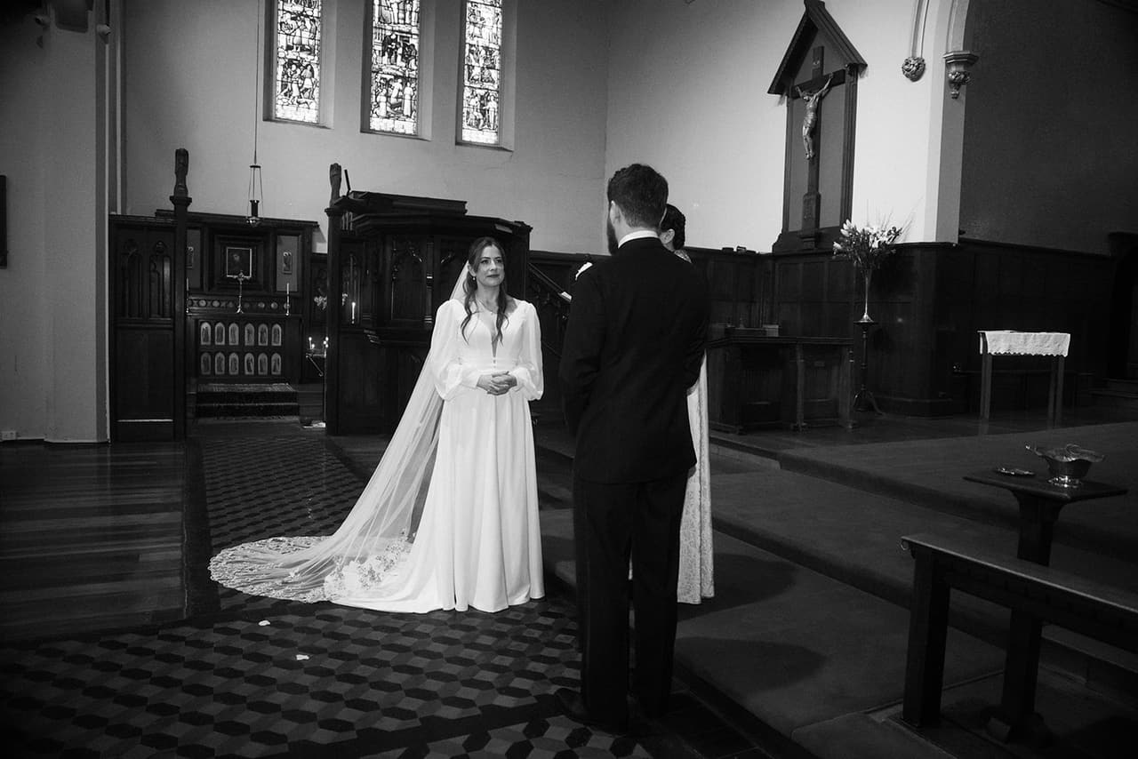 Black and white photo of Bianca and Aidan standing before the sanctuary, her long veil spread over the tiled floor