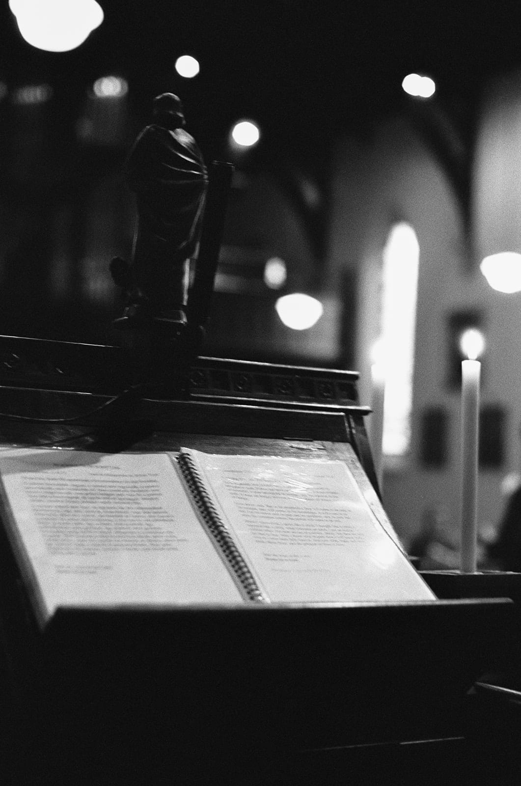 Black and white photo of an order of service lying open on a timber lectern in the church, on 35mm film